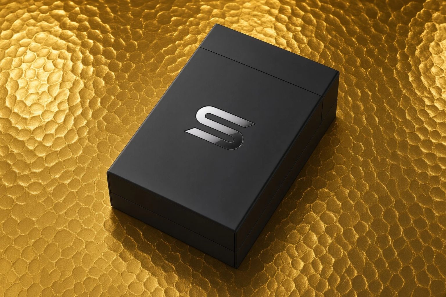 A matte black product box resting on a hammered gold surface